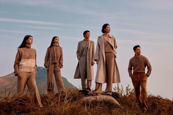 Fashion editorial featuring a group in neutral outfits against an open landscape