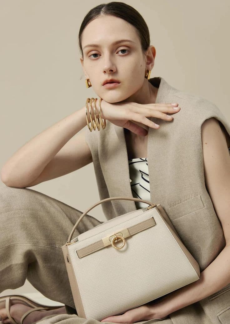 Portrait of a woman holding an ivory handbag with gold-tone details