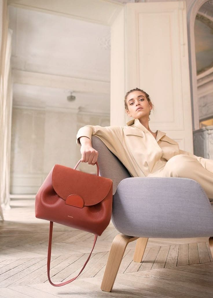 Woman seated in a light-filled room with a terracotta handbag