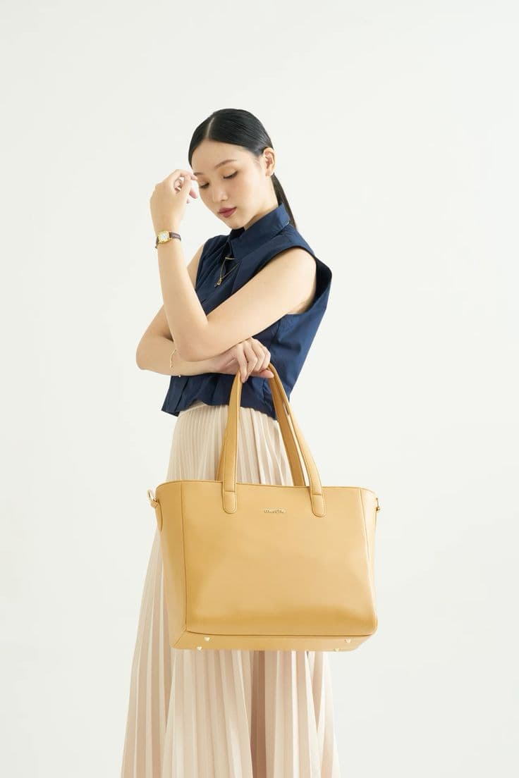 Woman carrying a golden yellow tote with a navy top and pleated skirt